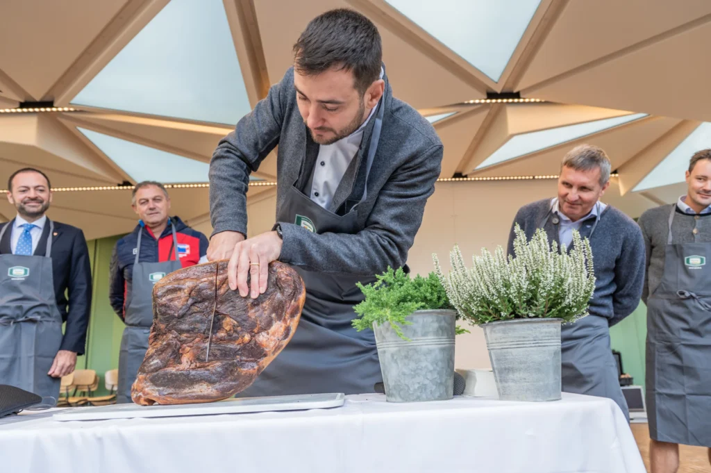 Vorführung des Speckanschnitts: Ein großer Südtiroler Speck wird auf einem Tisch fachgerecht geschnitten.