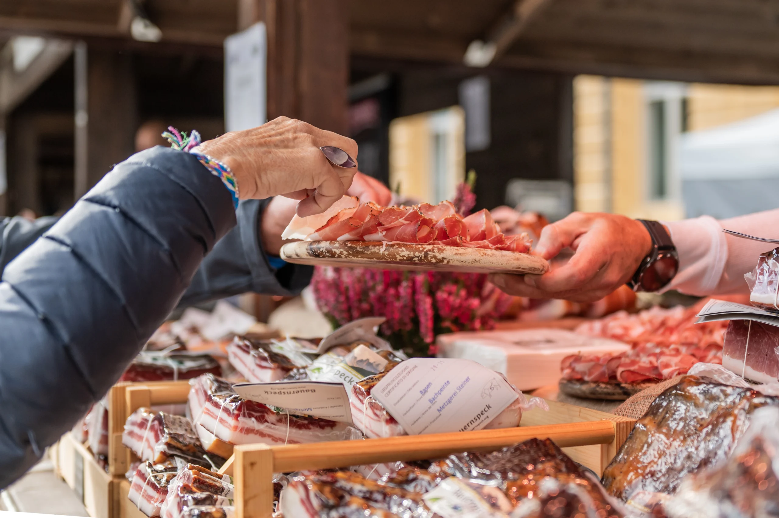 Übergabe eines Holzbretts mit frisch aufgeschnittenem Südtiroler Speck an einem Marktstand beim Speckfest.