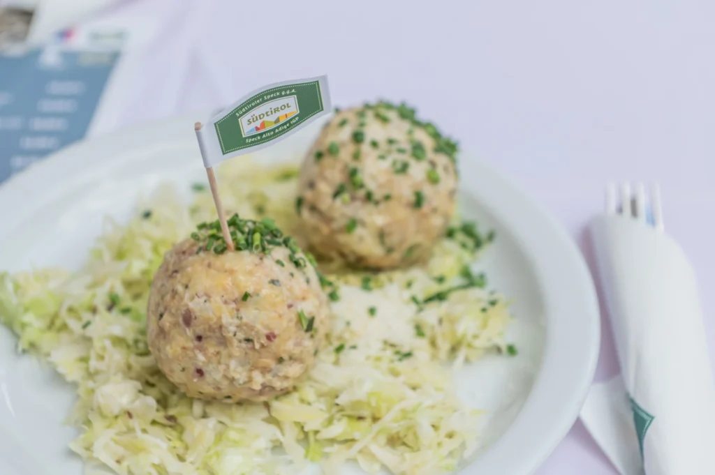 Zwei Südtiroler Speckknödel auf Sauerkraut, serviert auf einem weißen Teller.