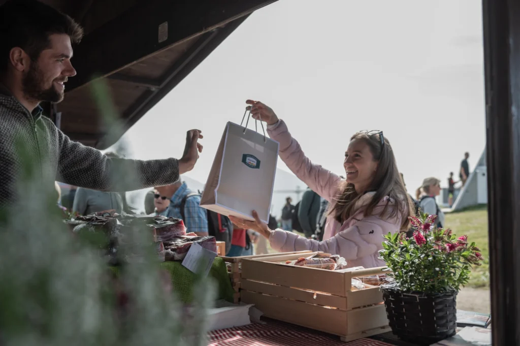 Kundin erhält eine Einkaufstasche mit Speckprodukten an einem Marktstand beim Speckfest am Kronplatz.