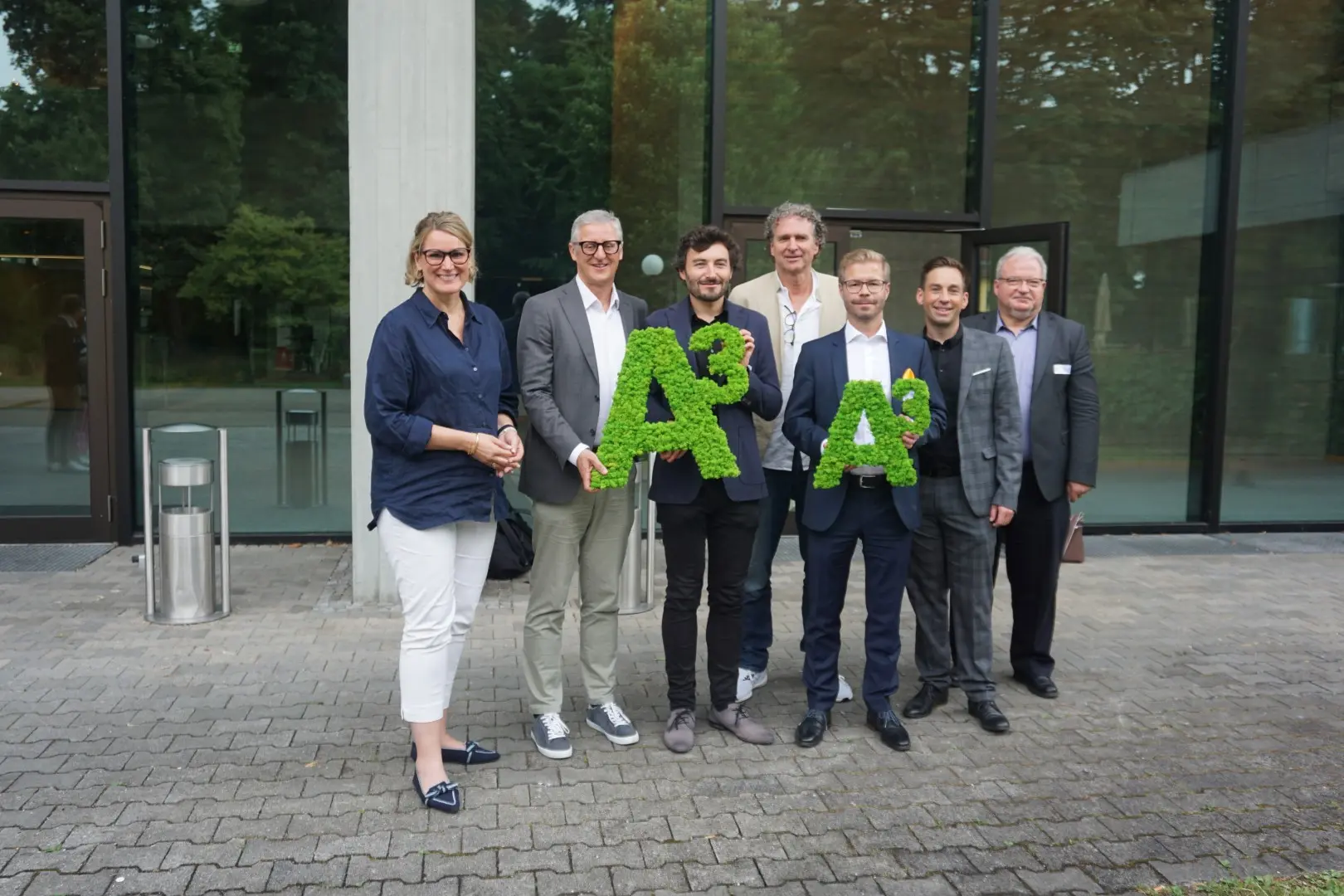 Gruppenfoto von Preisträgerinnen und Preisträgern mit grünen „A³“-Buchstaben bei der Verleihung des A³ Immobilien Awards vor einem modernen Gebäude.